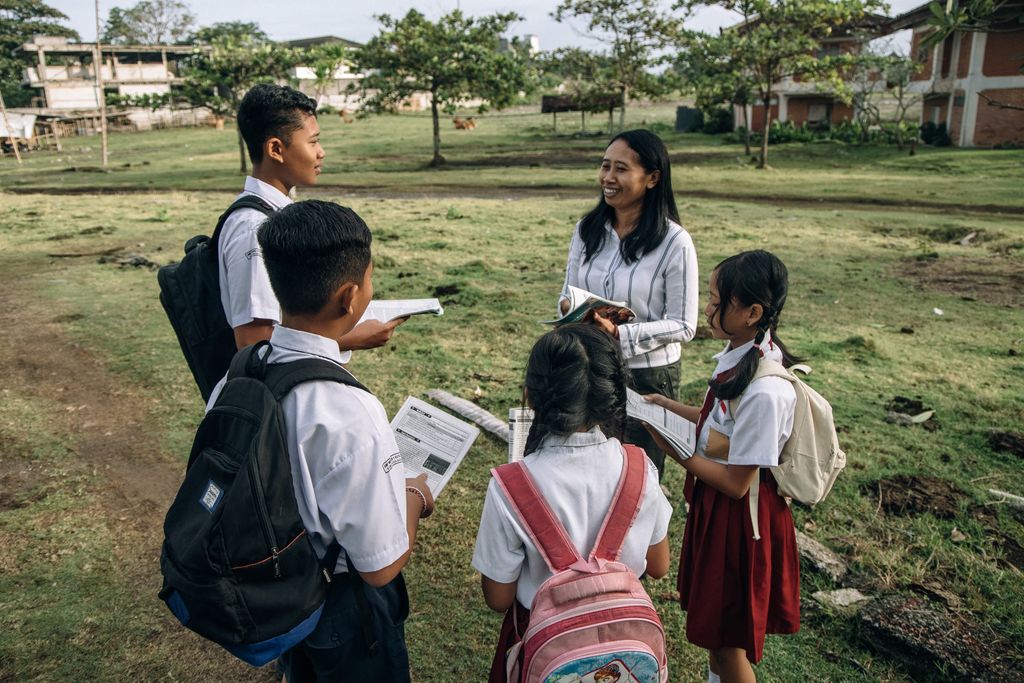A group of students in school uniforms learning outdoors with their teacher.